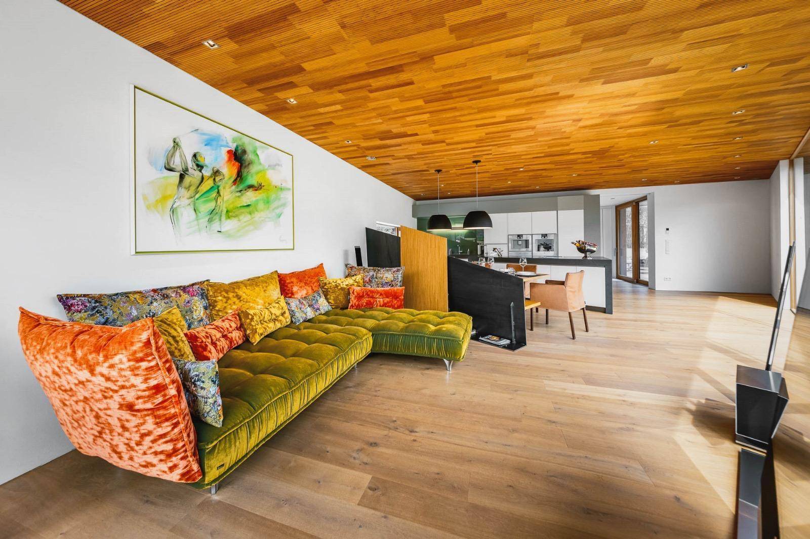 Farbenfrohes Wohnzimmer mit Samtsofa, Holzboden und offener Verbindung zur modernen Küche.