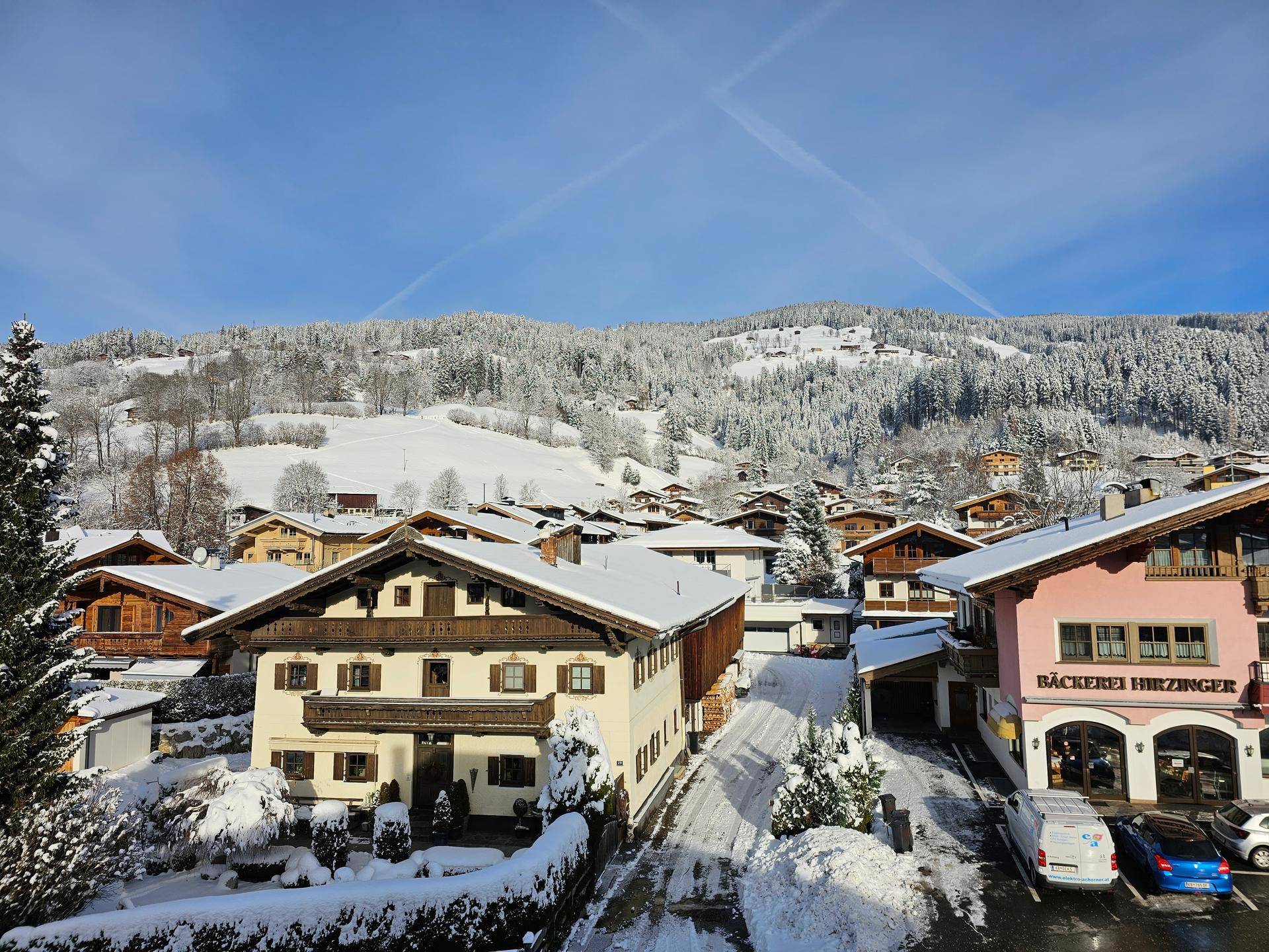 Panoramablick auf ein verschneites Dorf mit traditionellen Häusern und majestätischen Bergen im Hintergrund unter blauem Himmel.