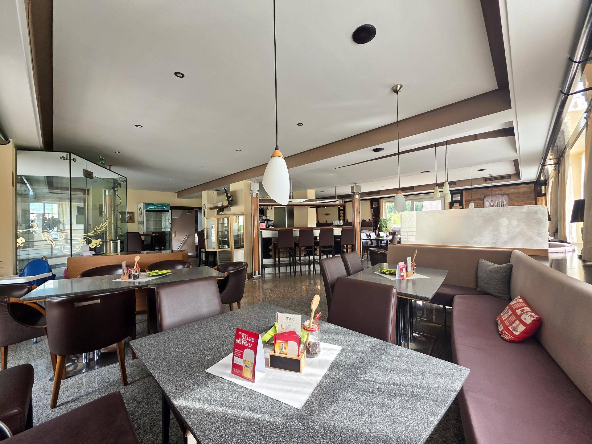Geräumiger Restaurantbereich mit Tischen, Stühlen, bequemen Sitzbänken und einer Bar im Hintergrund.