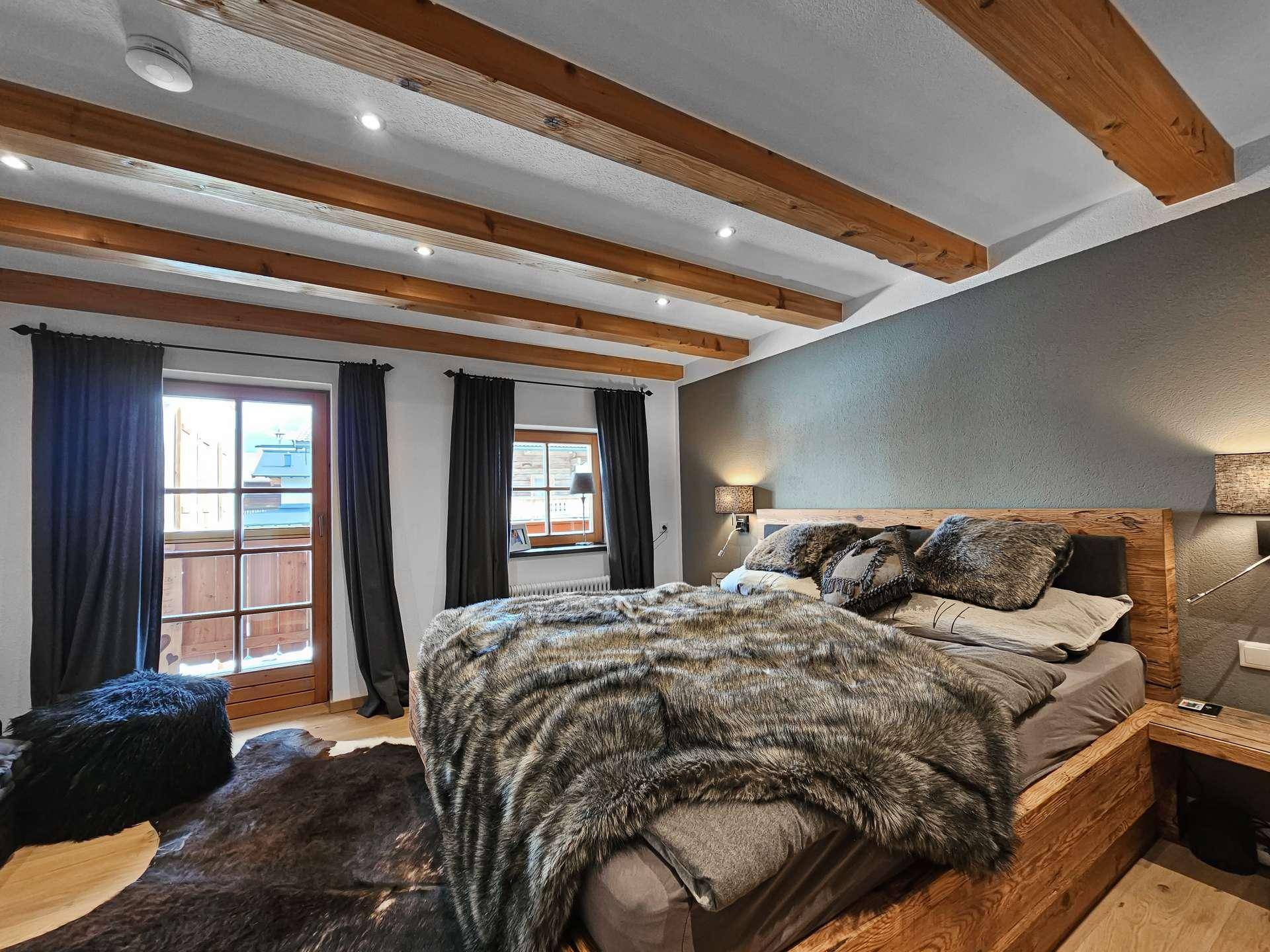 Helles Schlafzimmer mit Holzbalken, gemütlichem Bett und Zugang zu einem Außenbereich.