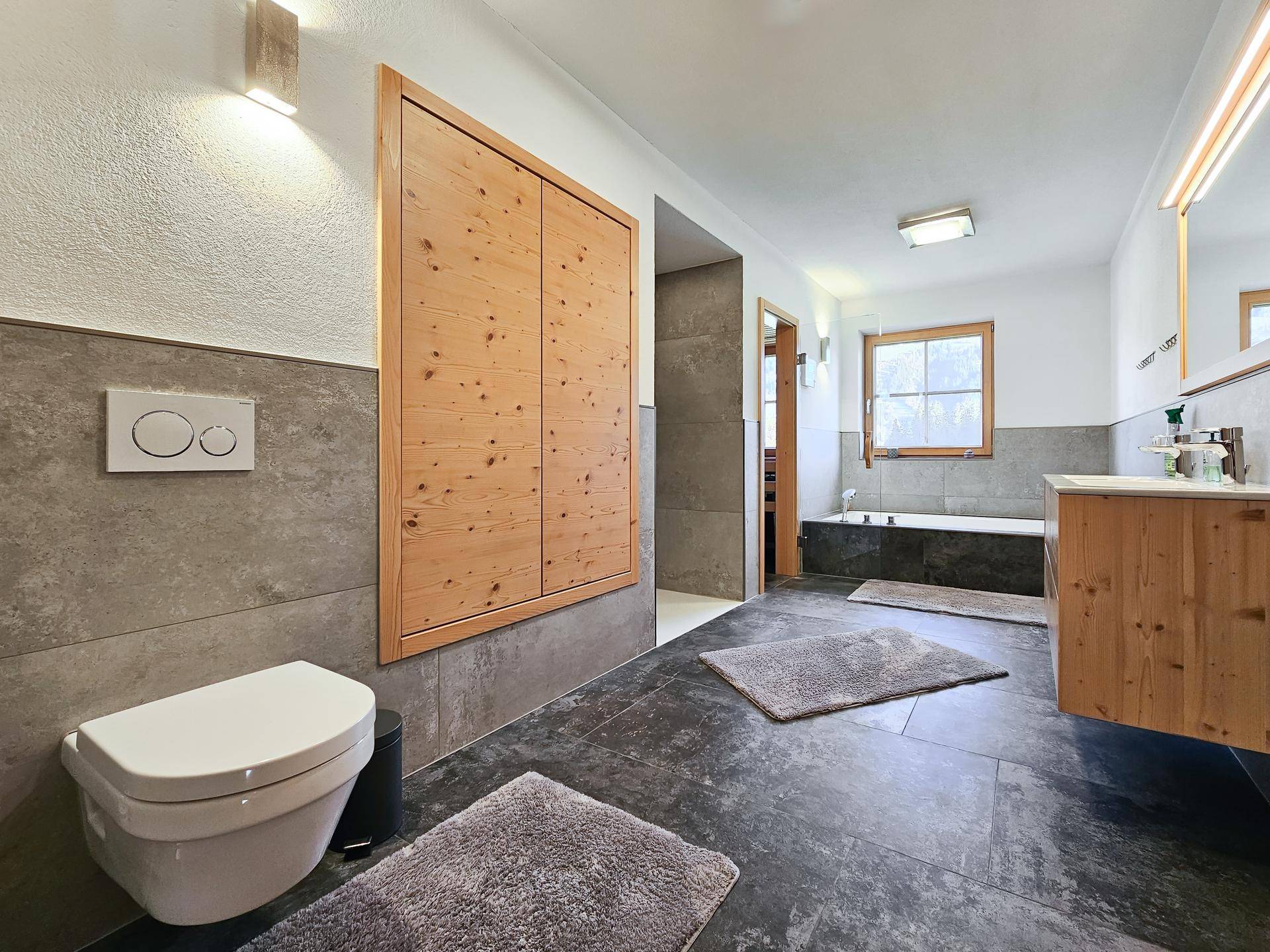 Geräumiges Badezimmer mit Wand-WC, Holzwaschtisch und großem Spiegel, ergänzt durch moderne Fliesen.