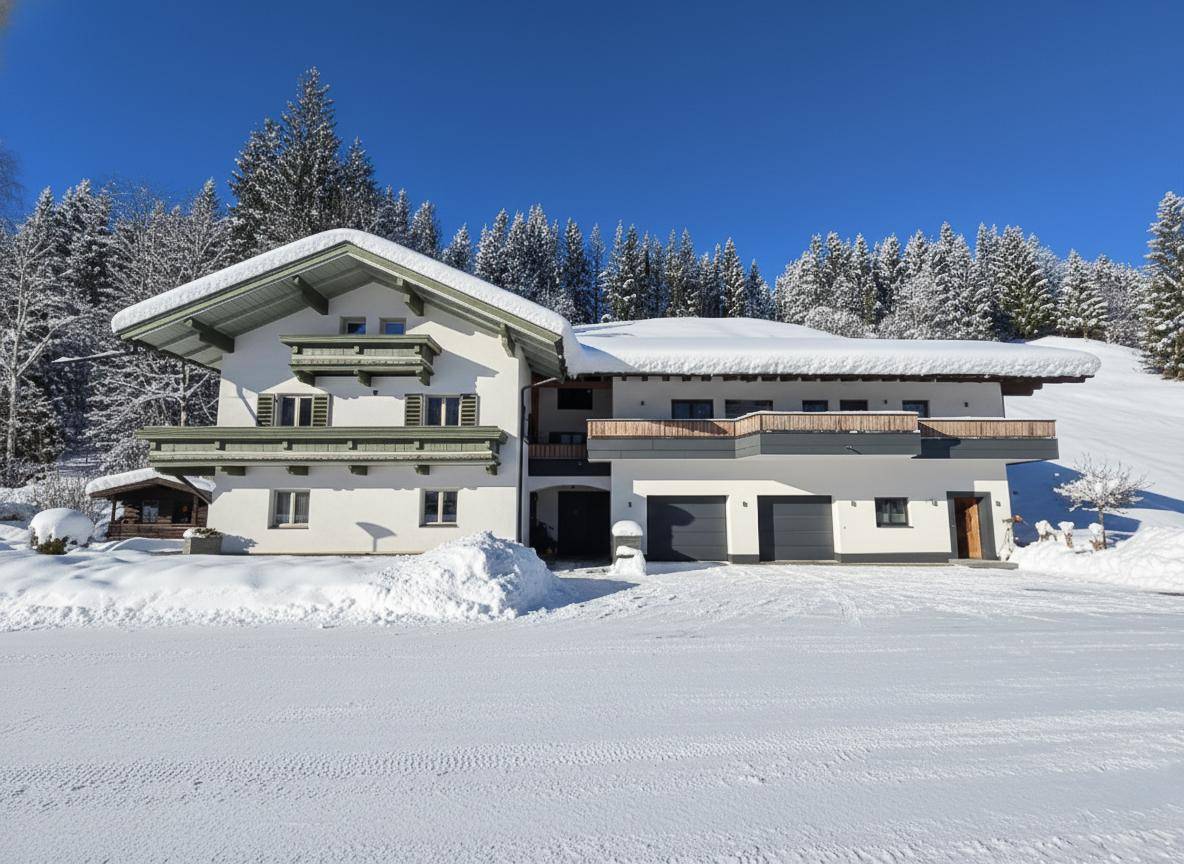 Großes Wohnhaus im alpinen Stil, umgeben von Schnee und Tannenbäumen unter blauem Himmel.
