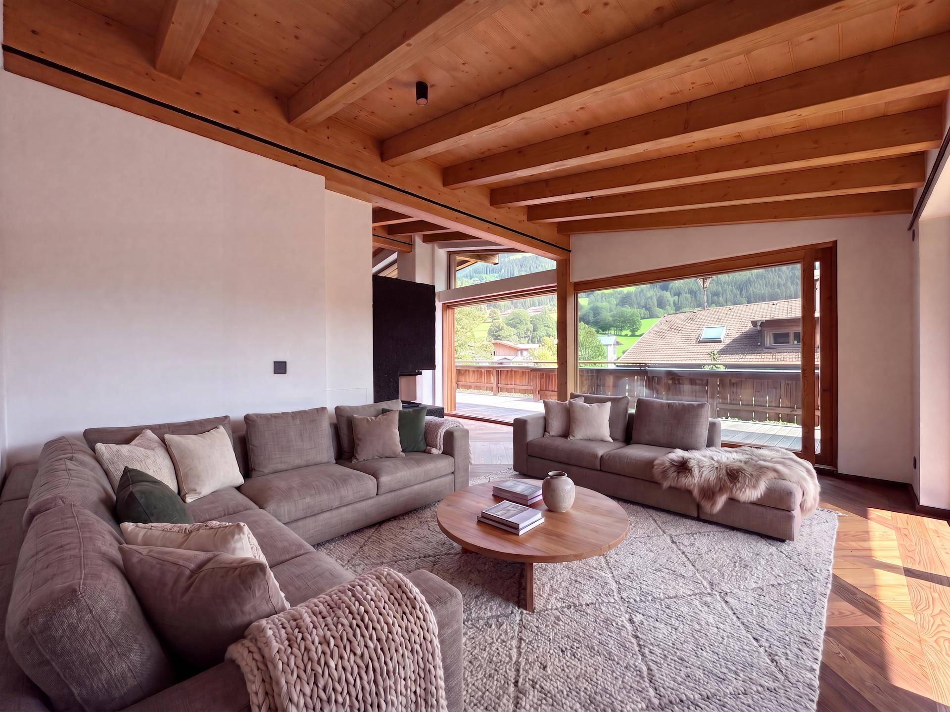 Gemütliches Wohnzimmer mit bequemen Sofas, Holzbalkendecke und weitem Blick auf die grüne Landschaft.