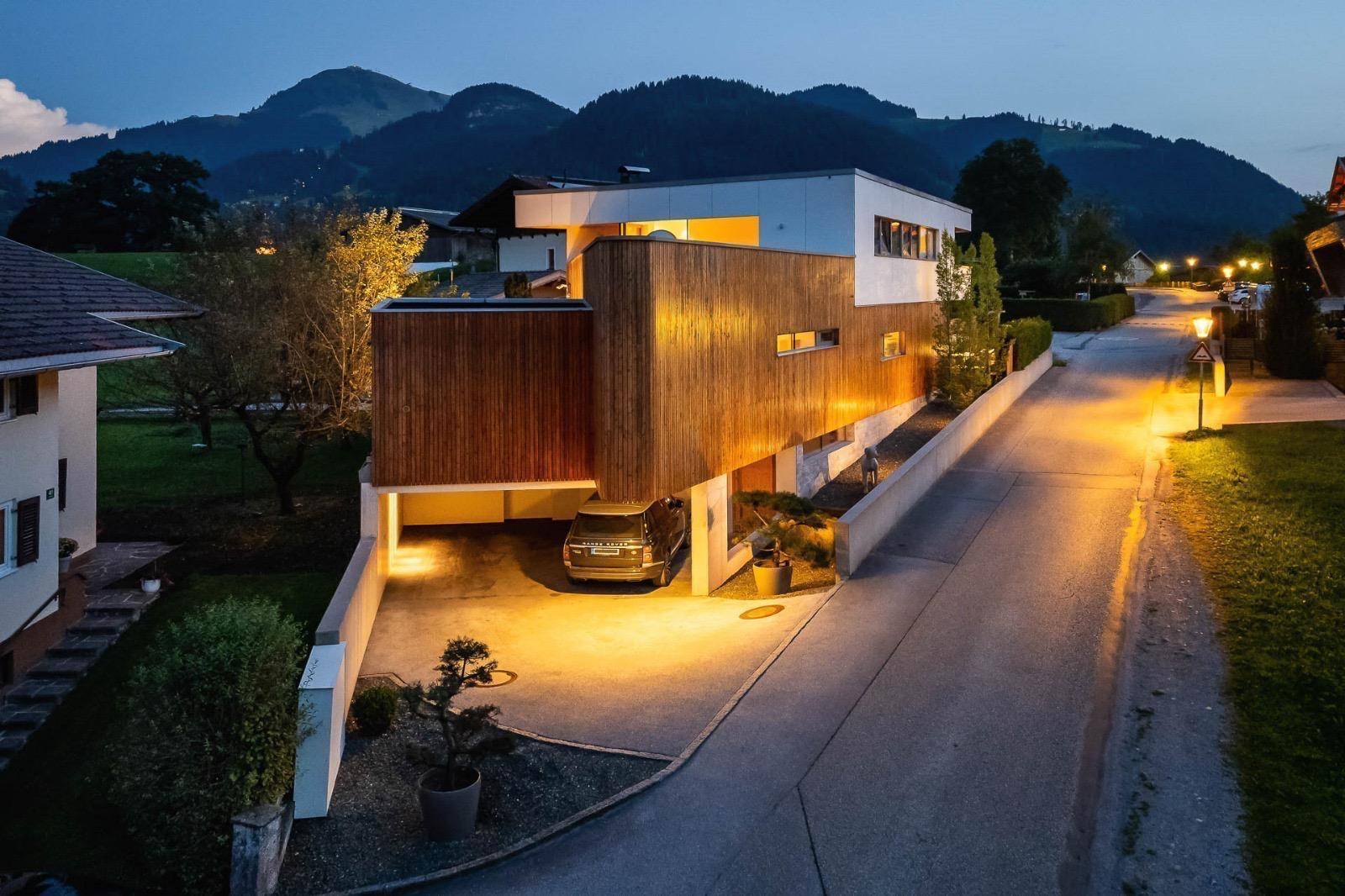 Modernes Wohnhaus mit Holzfassade und integrierter Garage, eingebettet in die ländliche Umgebung.
