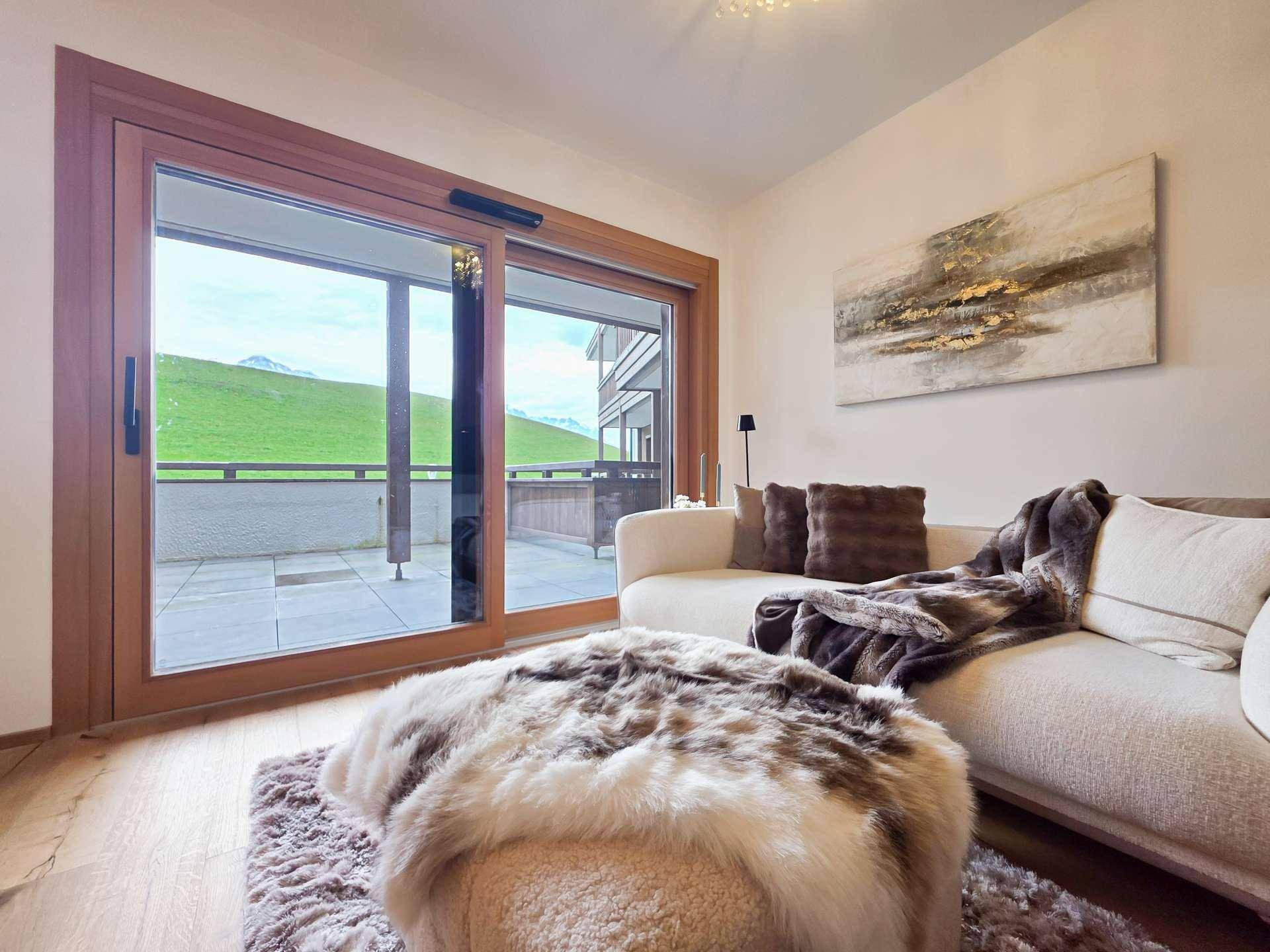 Heller Wohnbereich mit bequemer Couch und großem Fenster mit Blick auf die grüne Landschaft.