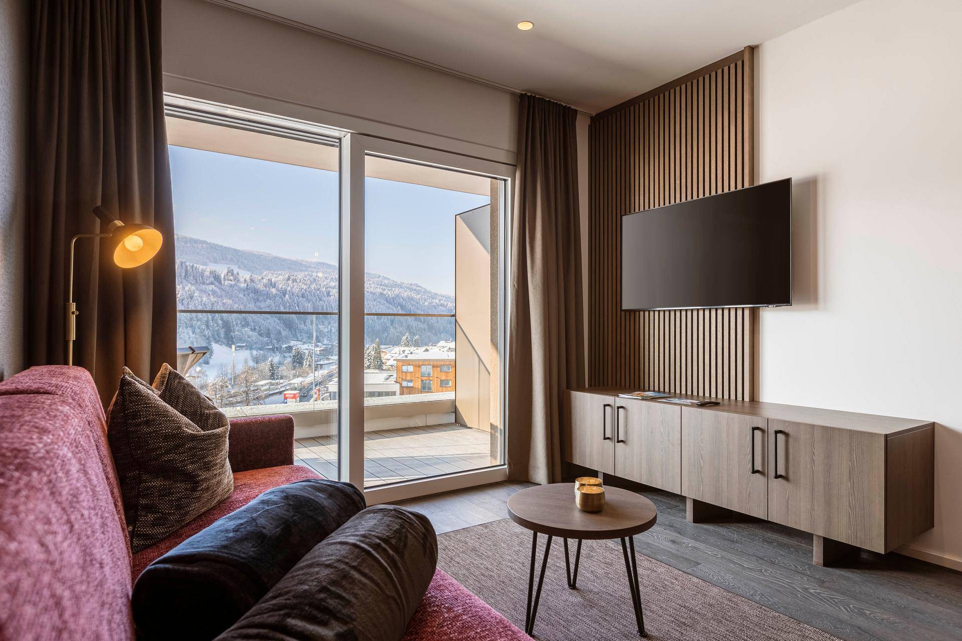 Gemütliches Wohnzimmer mit Sofa, Fernseher und Zugang zu einem Balkon mit Bergblick.