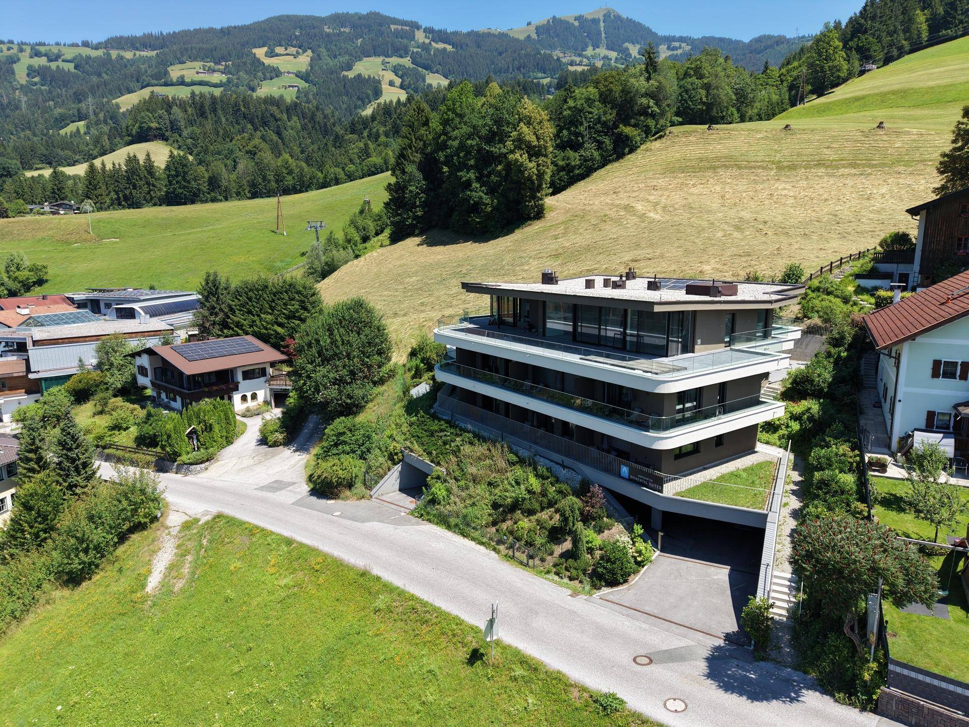 Moderne Wohnanlage in einer grünen Hügellandschaft, umgeben von Natur und anderen Häusern.
