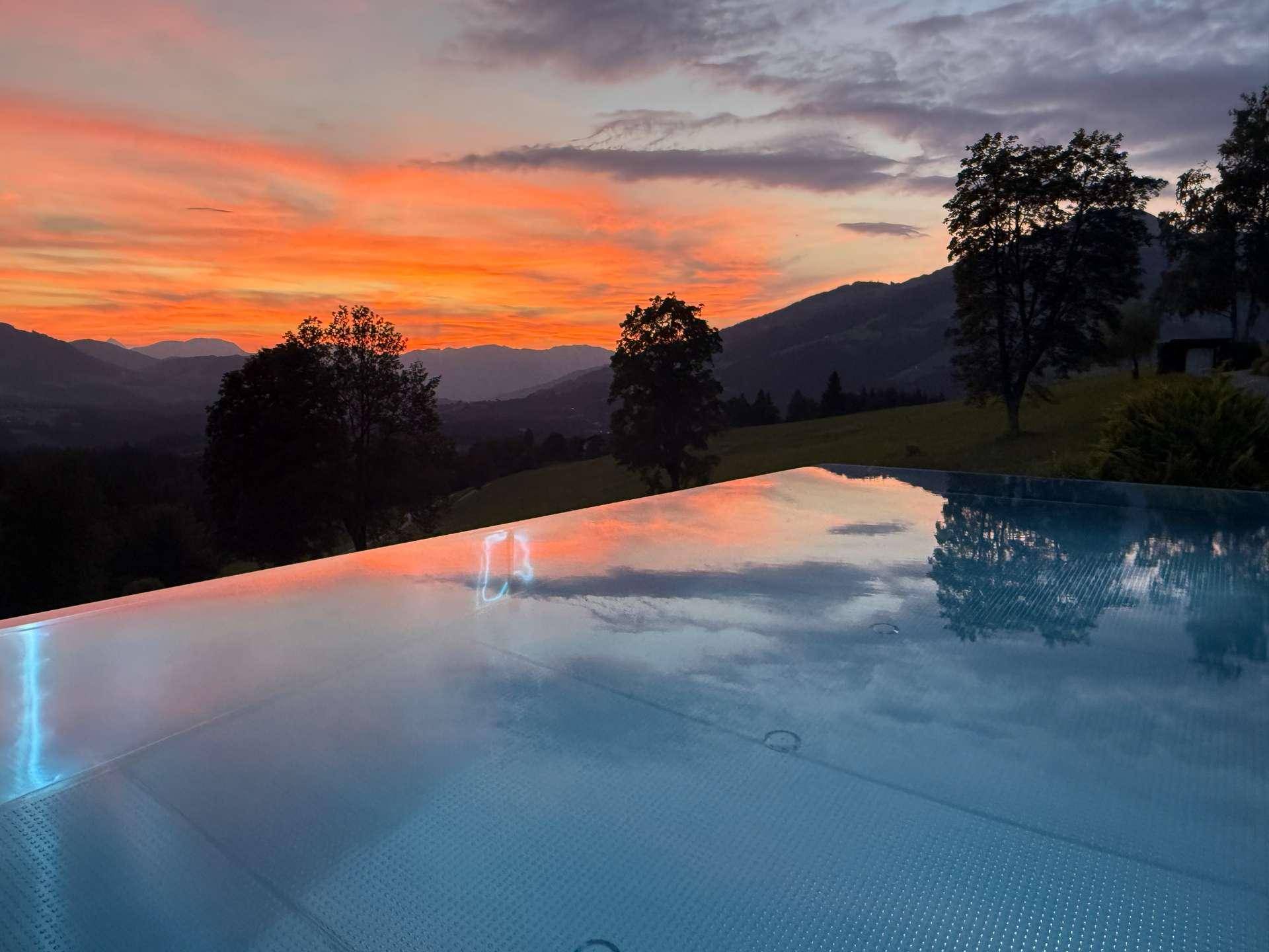 Infinity-Pool bei Sonnenuntergang mit spektakulärem Blick auf die umliegende Berglandschaft.