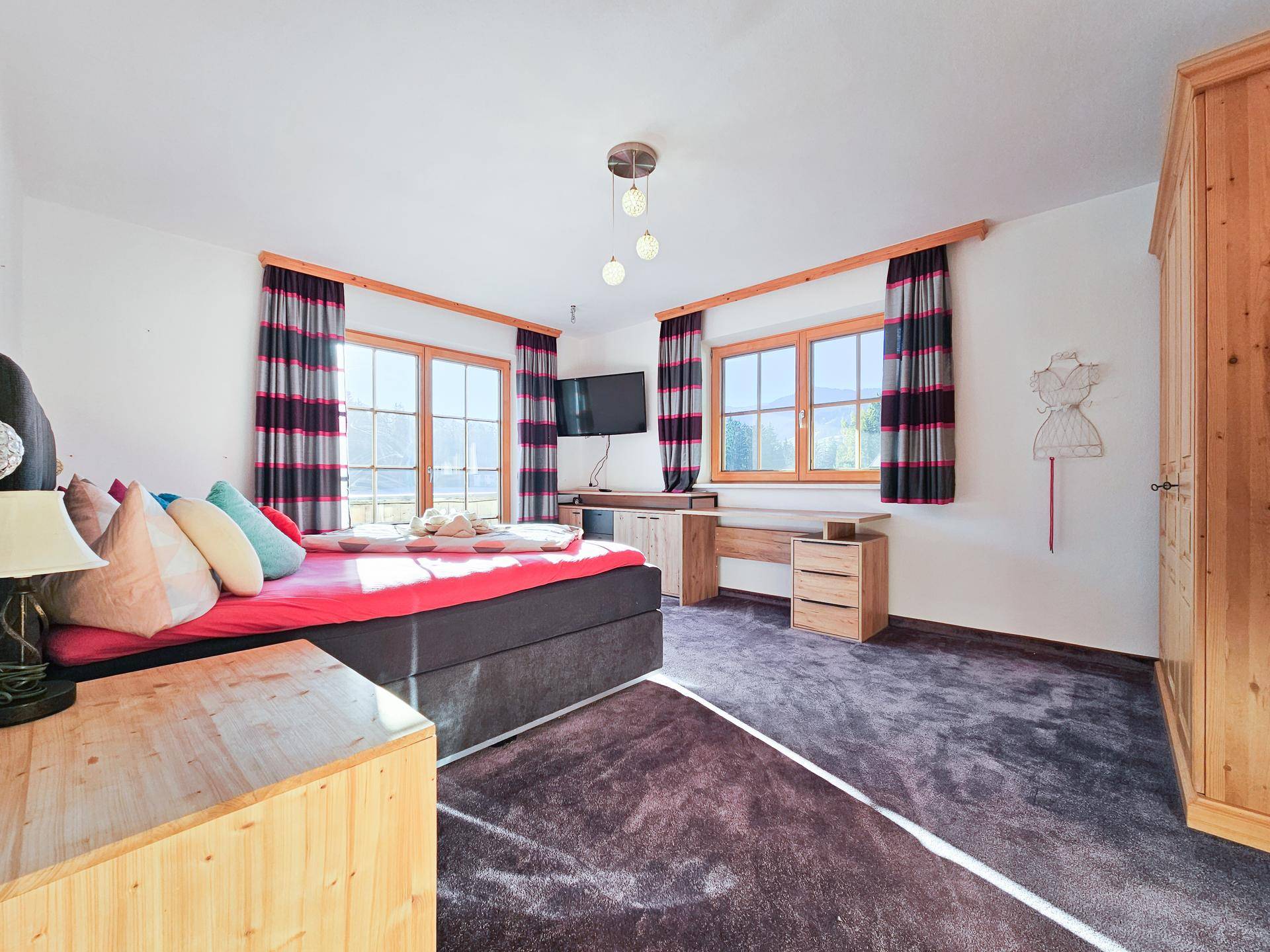 Gemütliches Schlafzimmer mit Teppichboden, Doppelbett, Fernseher und Schreibtisch, mit Blick auf die Berge.