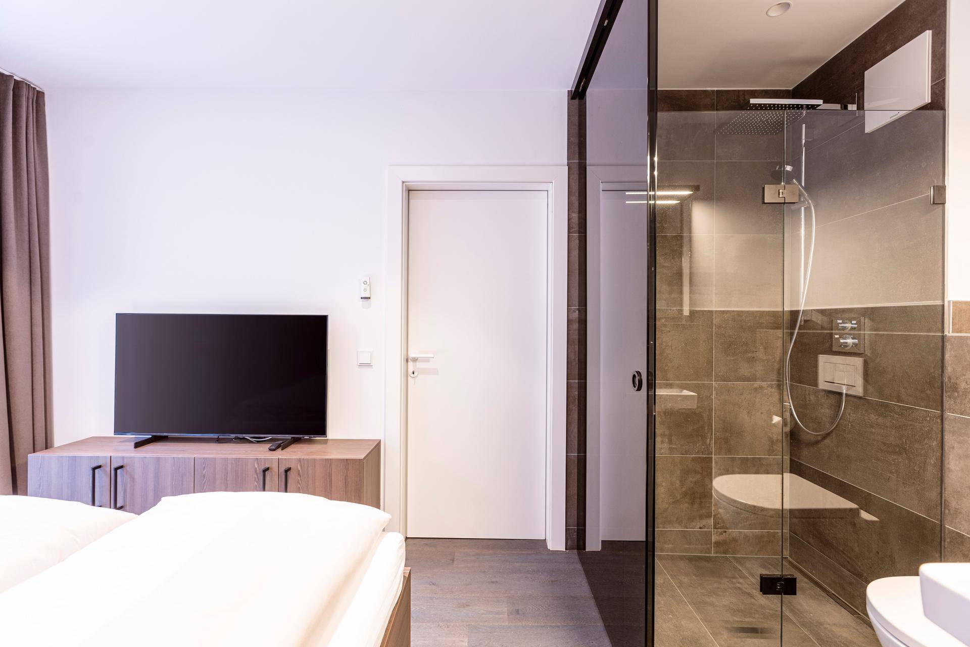 Schlafzimmer mit Doppelbett und modernem Bad mit Dusche, abgetrennt durch Glaswand.