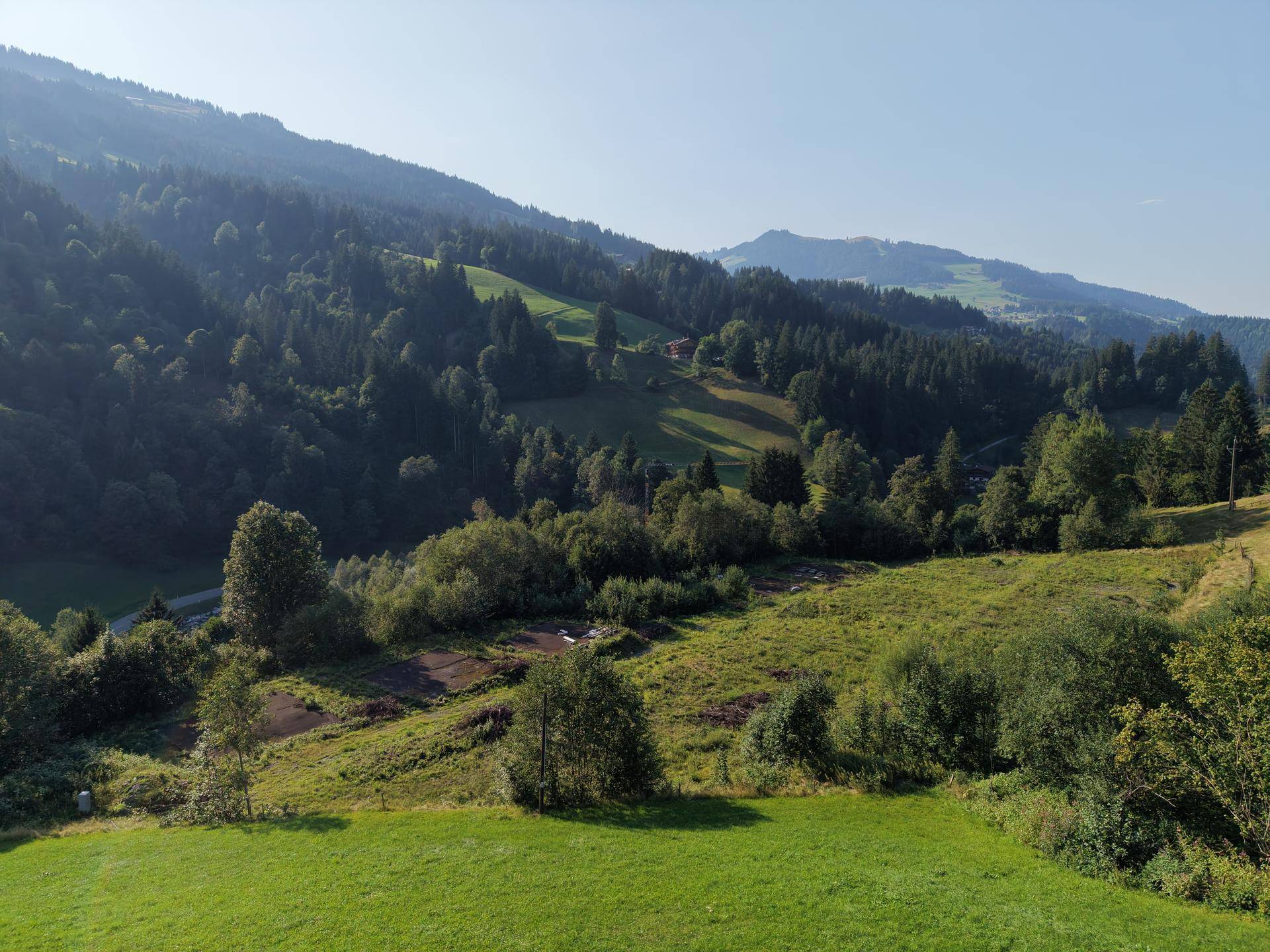 Weitläufiger Blick über grüne Wiesen und bewaldete Hügel unter einem klaren blauen Himmel.