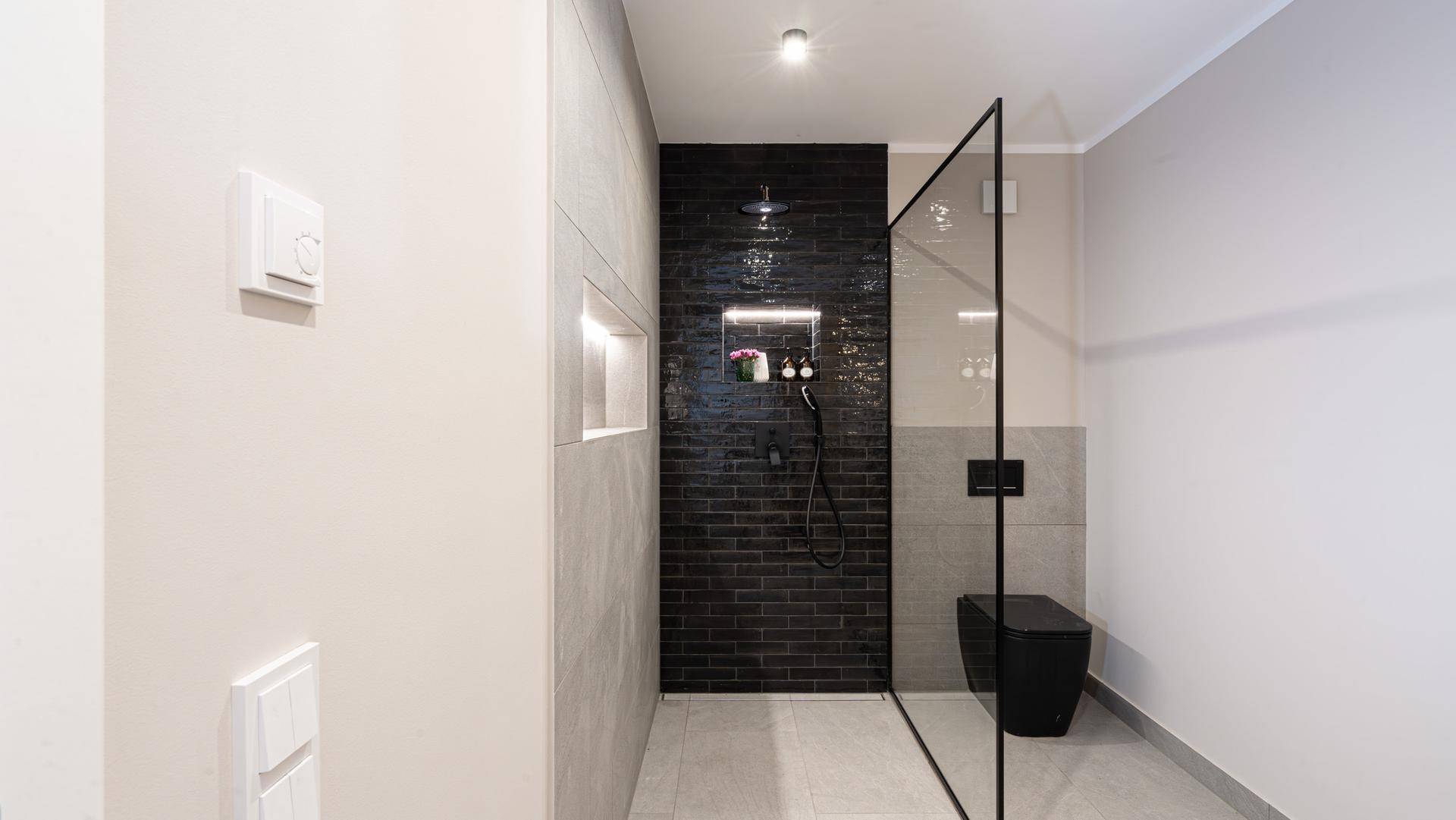 Elegantes Badezimmer mit begehbarer Dusche, schwarzer Wandverkleidung und wandhängendem WC.