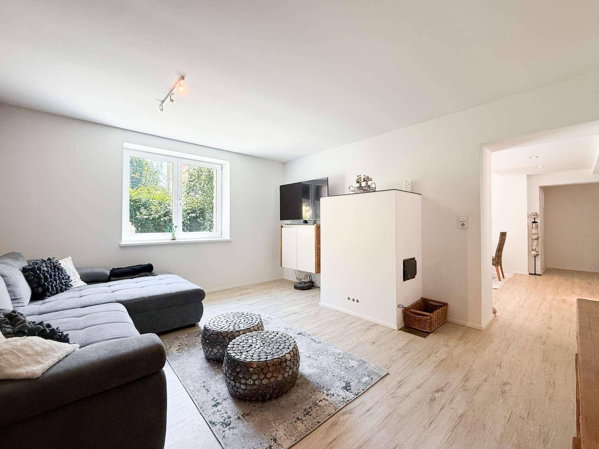 Helles Wohnzimmer mit grauem Ecksofa, Kamin und Blick ins Grüne.