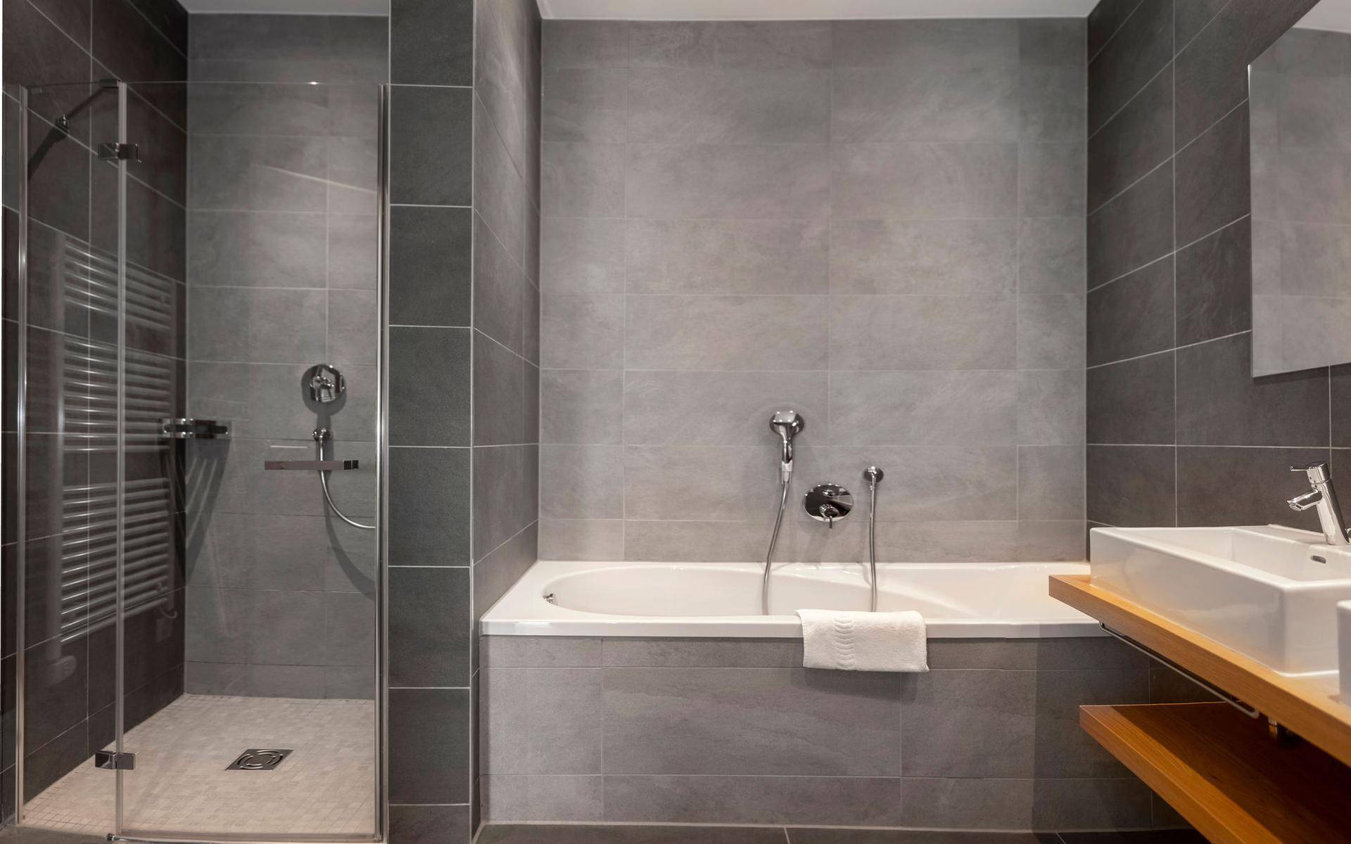 Modernes Badezimmer mit grauen Fliesen, Badewanne, ebenerdiger Dusche und Einzelwaschbecken.