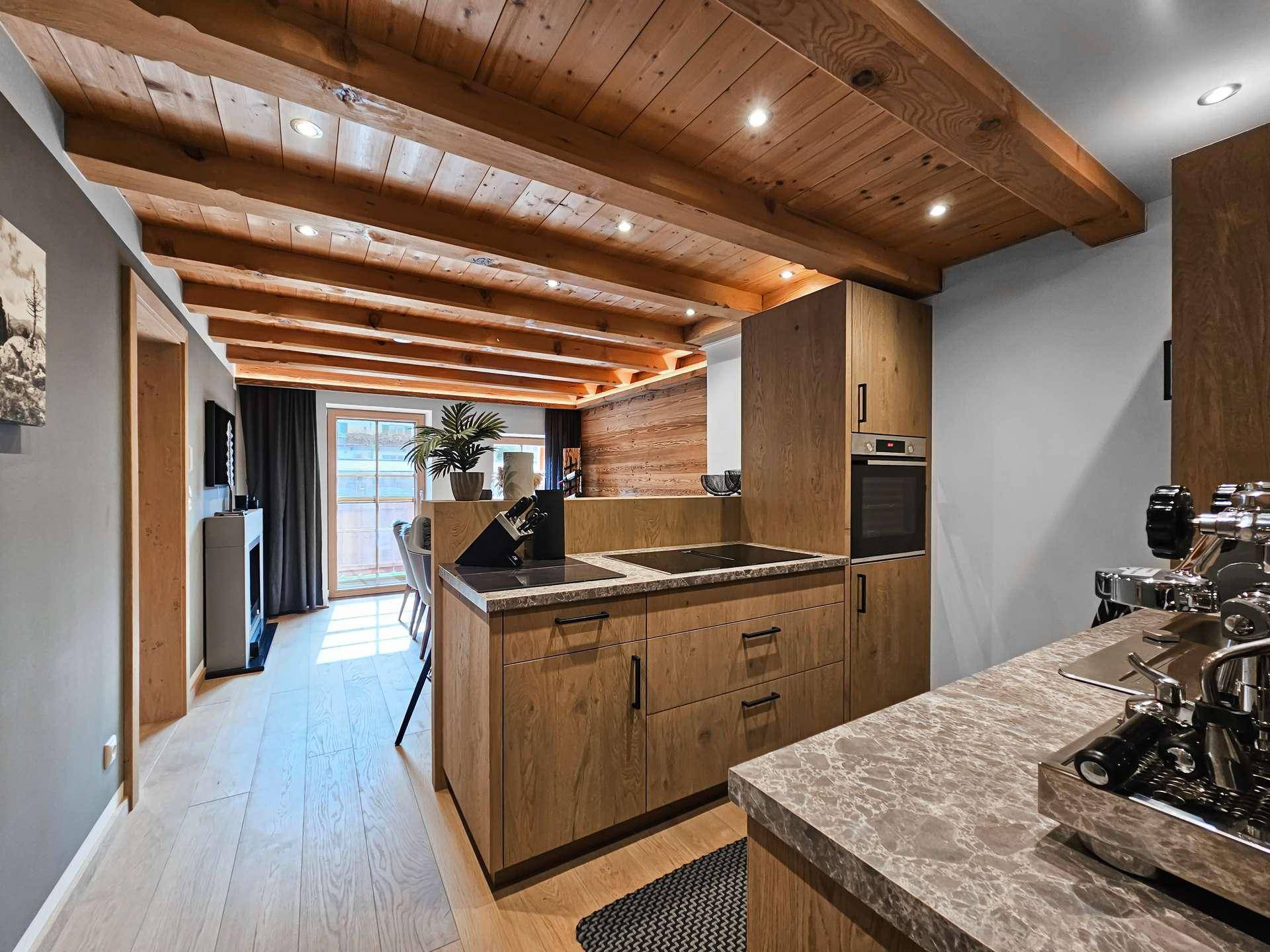Moderne Küche mit Holzfronten, dunkler Arbeitsplatte und integrierten Geräten in offenem Wohnbereich.