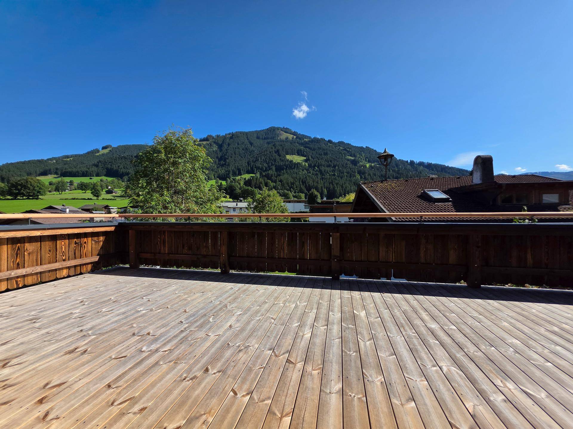 Weitläufige Holzterrasse mit unverbautem Blick auf die umliegenden Berge und das Tal.