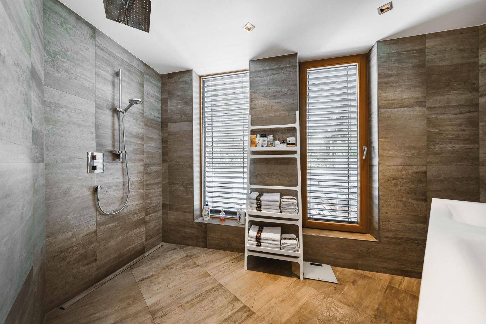 Geräumige begehbare Dusche mit Regenduschkopf und großen Fliesen in einem modernen Badezimmer.