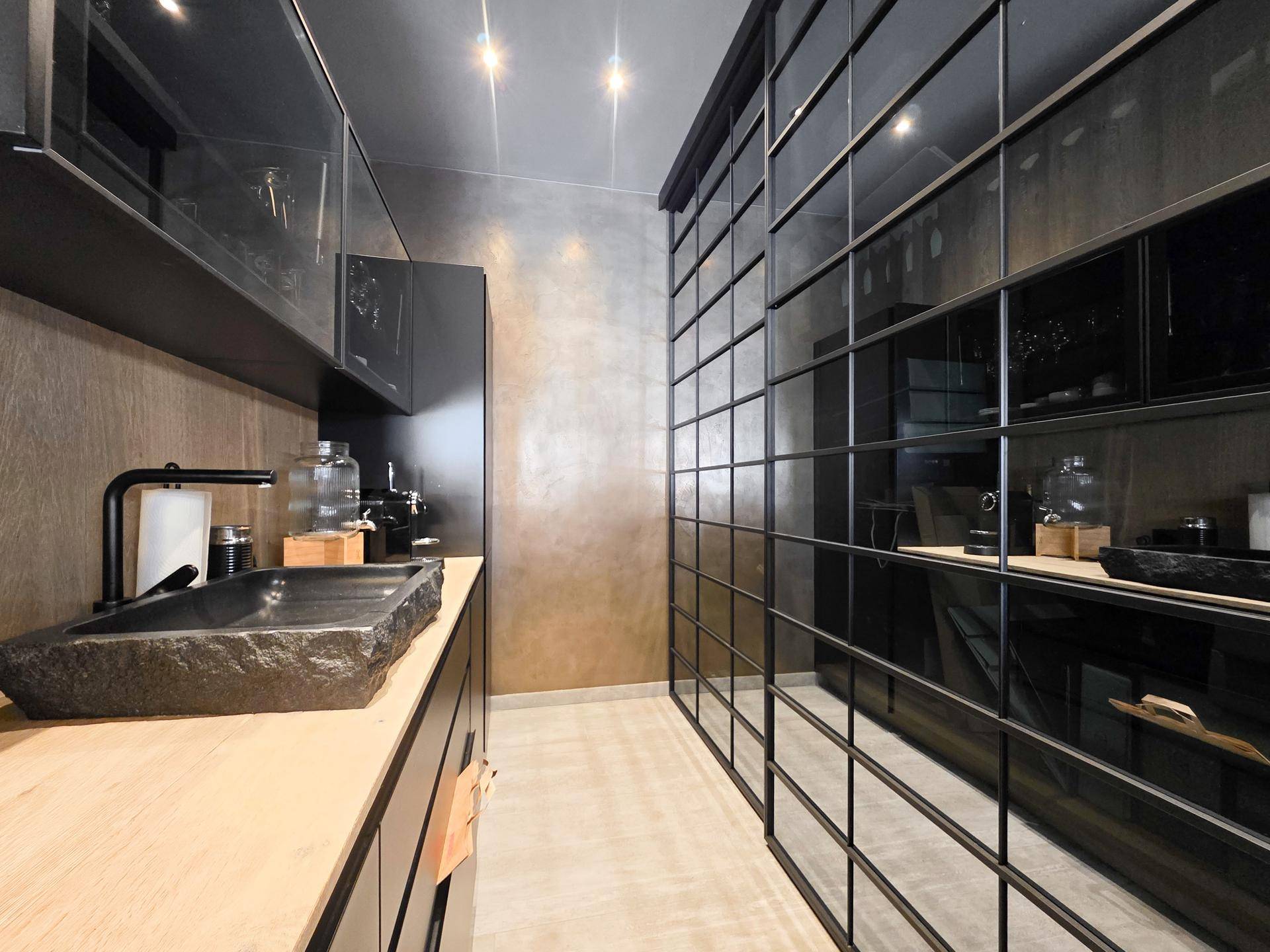 Modernes Badezimmer mit dunklen Schränken, einem Steinwaschbecken und einer eleganten Glaswand als Raumteiler.