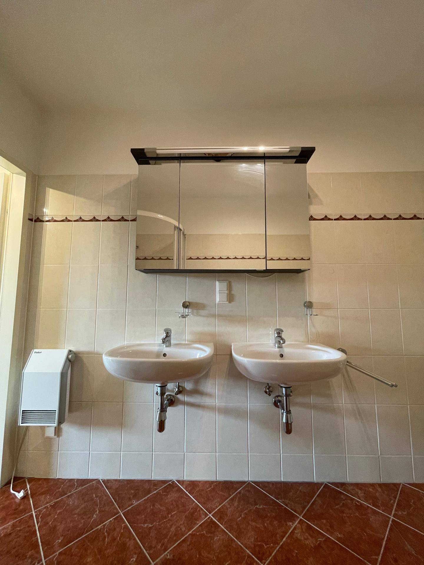 Badezimmer mit Doppelwaschbecken, Spiegelschrank und Wandheizung.