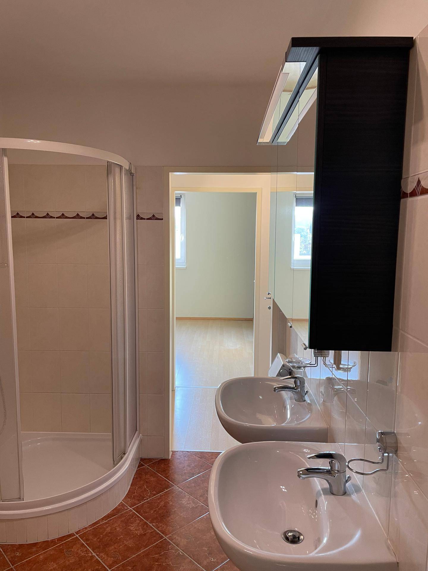 Badezimmer mit Doppelwaschbecken, Spiegelschrank und Duschkabine.