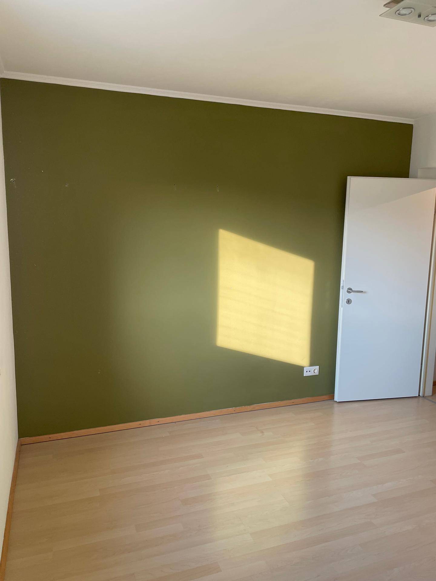 Schlafzimmer mit einer grünen Akzentwand und hellem Laminatboden.