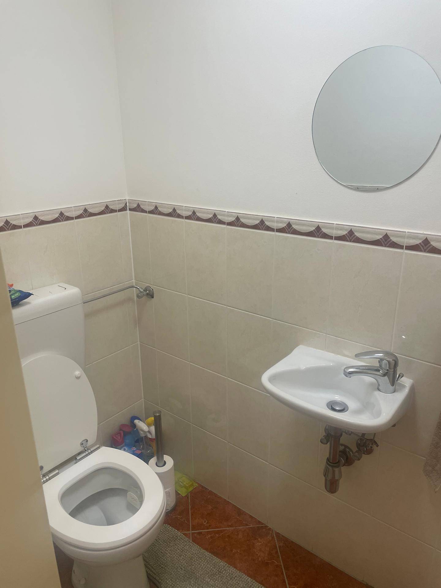 Gäste-WC mit Toilette, kleinem Waschbecken und runden Spiegel über den Fliesen.