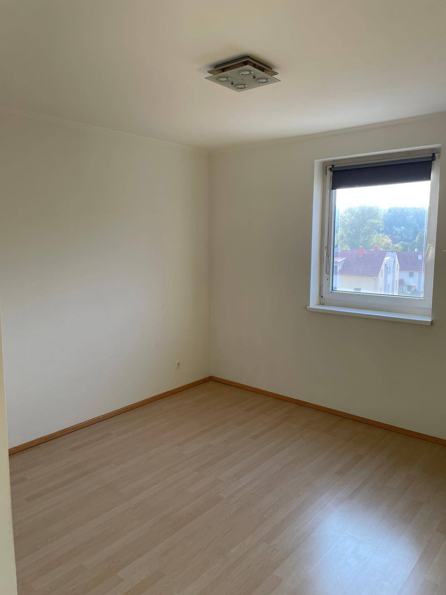 Leeres Schlafzimmer mit hellem Laminatboden und einem Fenster.