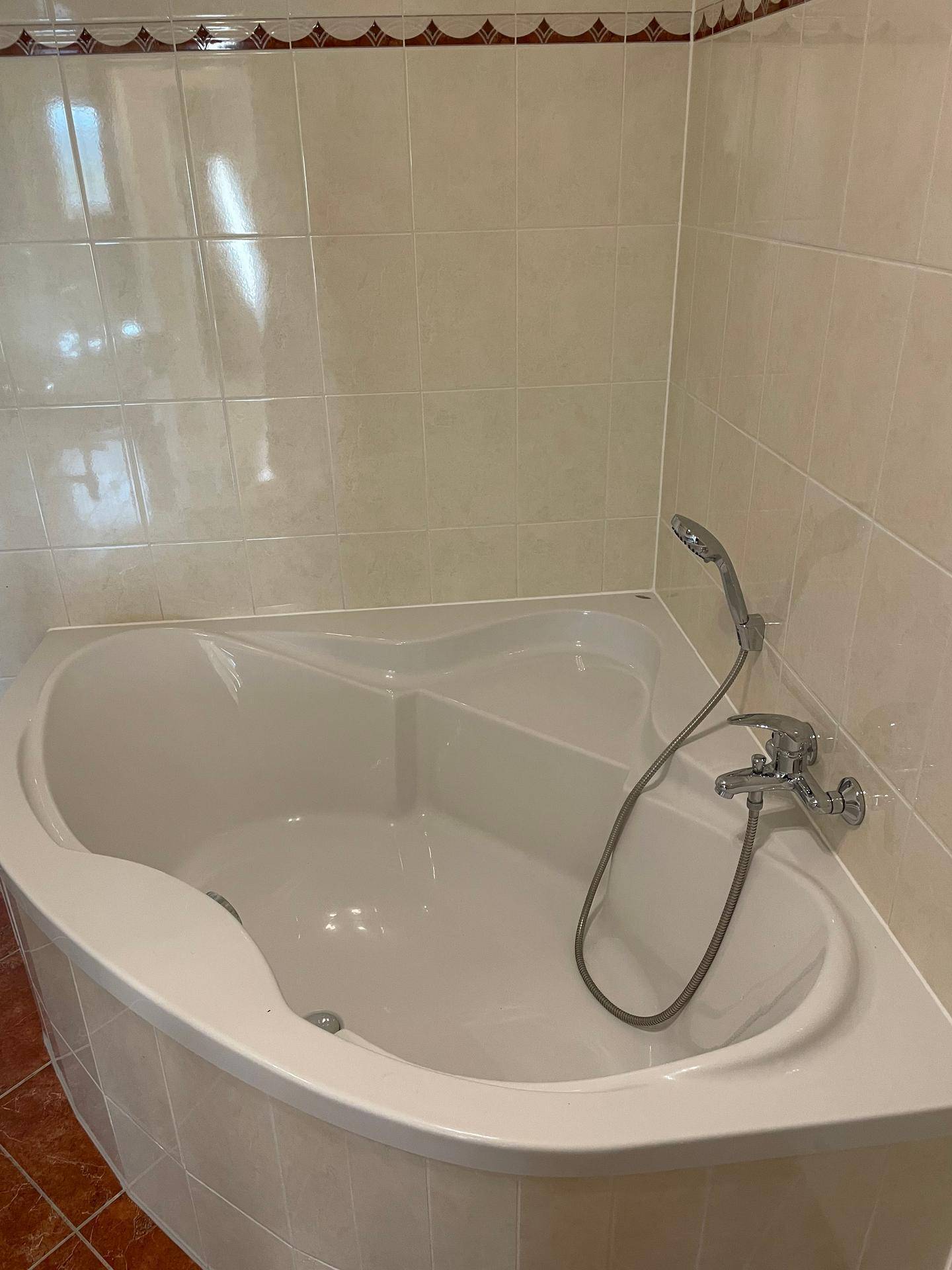 Eckbadewanne mit Duscharmatur in einem gefliesten Badezimmer.