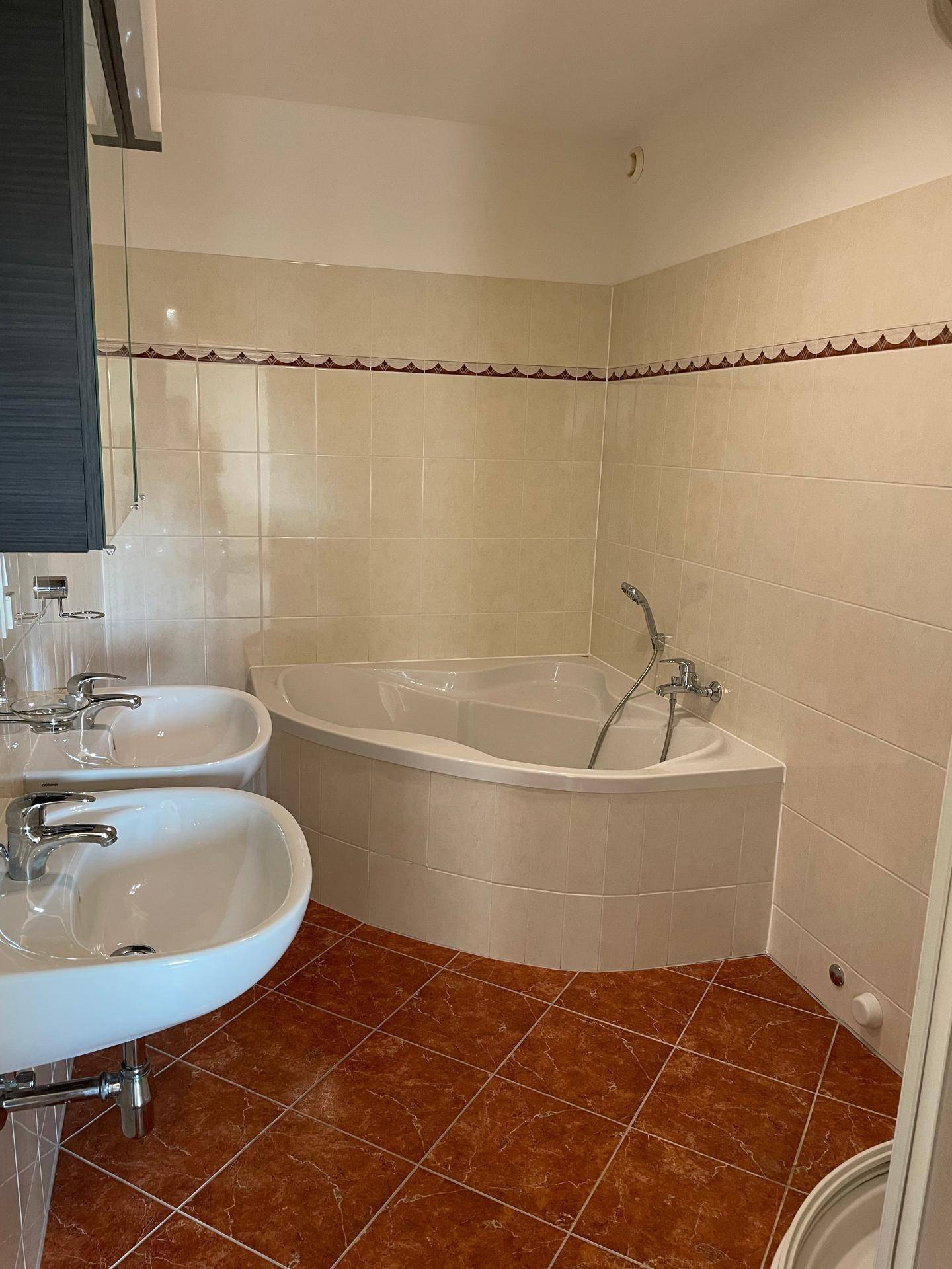 Badezimmer mit zwei Waschbecken, Eckbadewanne und hellen Fliesen.