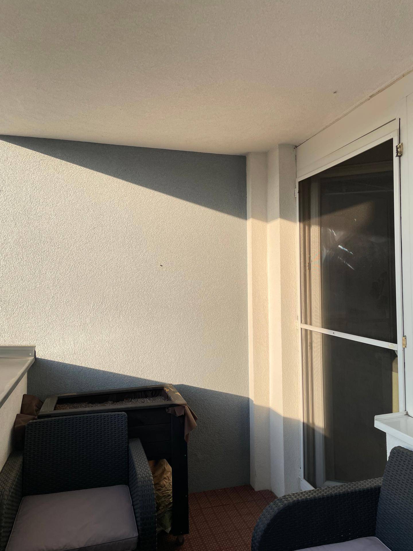 Überdachter Balkon mit Sitzgelegenheiten und Grill, teilweise von der Sonne beschienen.