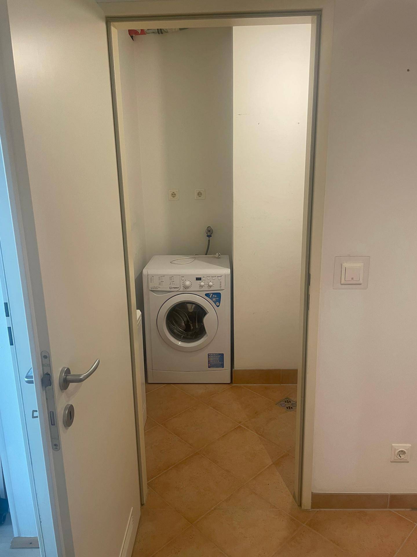 Hauswirtschaftsraum mit Waschmaschine und Terrakotta-Fliesenboden.
