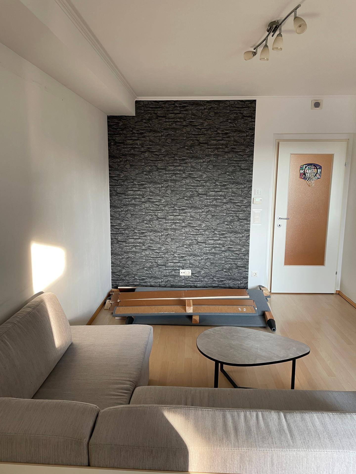 Wohnzimmer mit dunkler Steinoptik-Akzentwand und hellem Laminatboden.