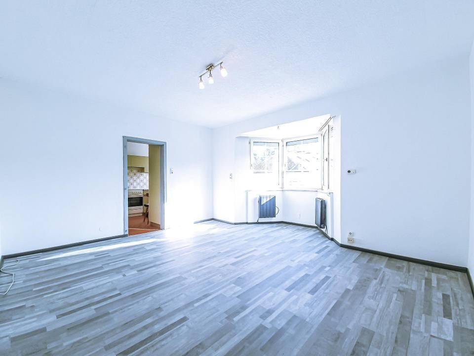 Geräumiges Wohnzimmer mit Erkerfenster, Laminatboden und Zugang zu einem weiteren Raum.