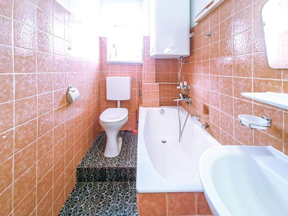 Badezimmer mit rosafarbenen Fliesen, Badewanne, Toilette und Fenster.