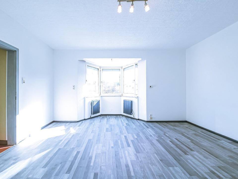 Helles, leeres Wohnzimmer mit Erkerfenster und modernem Laminatboden.