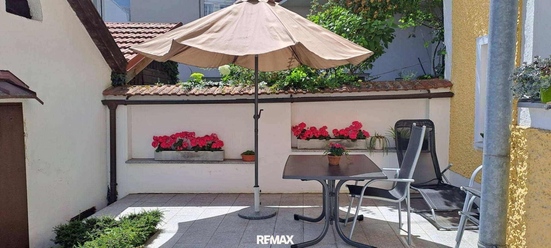 Gemütliche Terrasse mit Sonnenschirm, Gartenmöbeln und Blumenkästen an der Wand für entspannte Stunden.