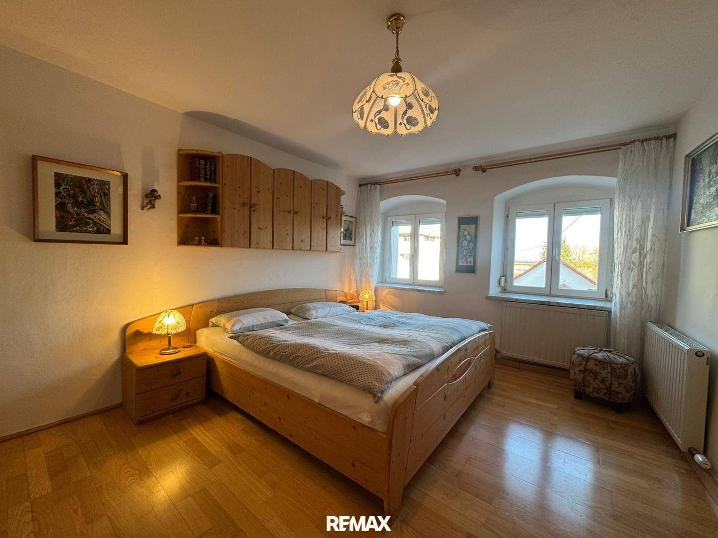 Gemütliches Schlafzimmer mit Holzmöbeln, Parkettboden und zwei Fenstern für viel Tageslicht.