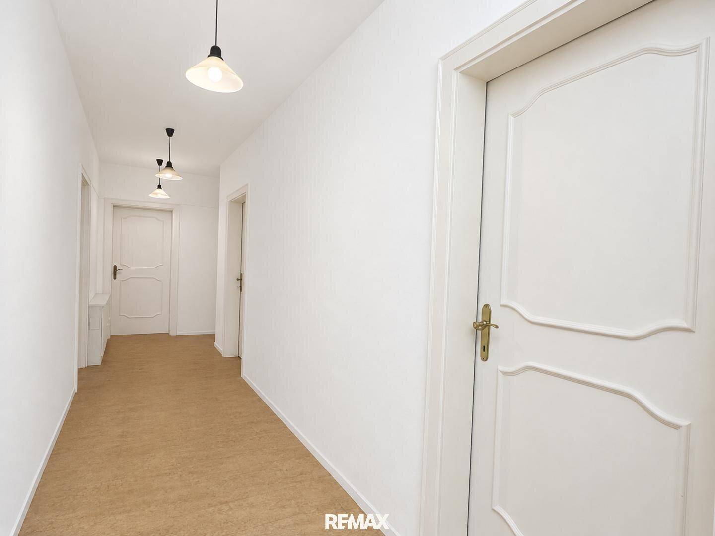 Heller Flur mit weißen Wänden, mehreren Türen und schlichtem Bodenbelag.