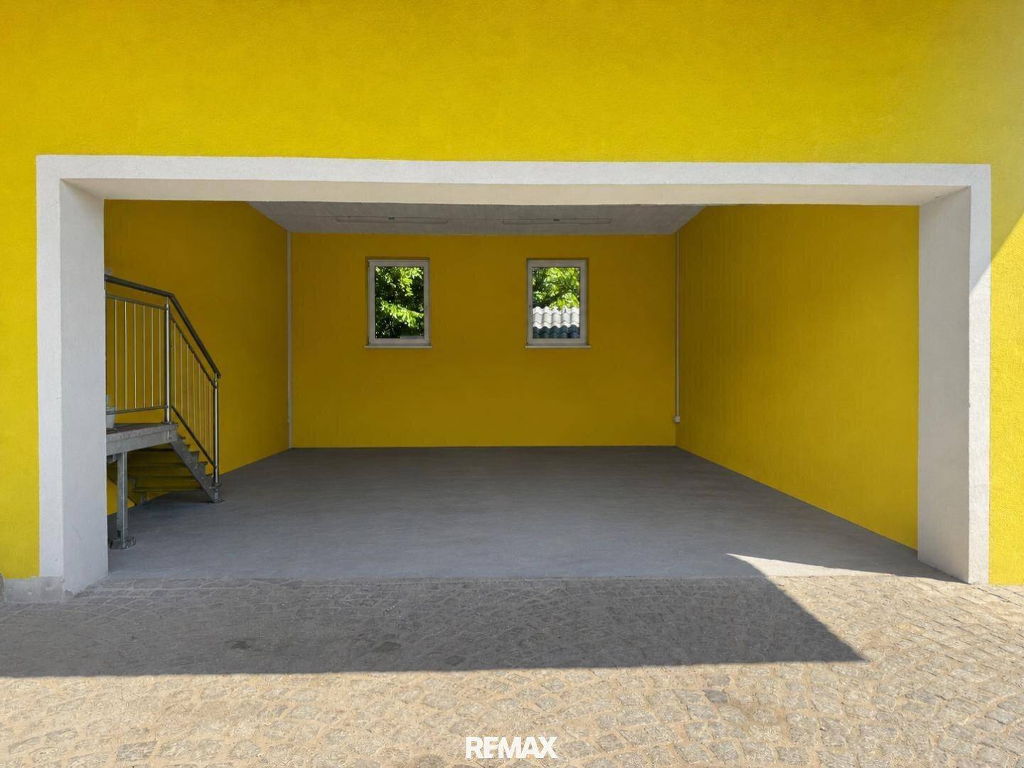 Leere Garage mit gelben Wänden, zwei Fenstern und Zugang zur Treppe.
