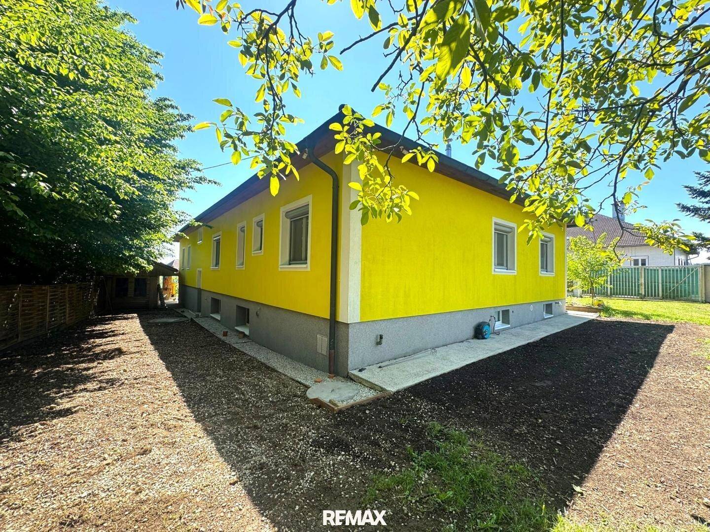 Seitenansicht des gelben Hauses mit vorbereitetem Gartenbereich und viel Grün.