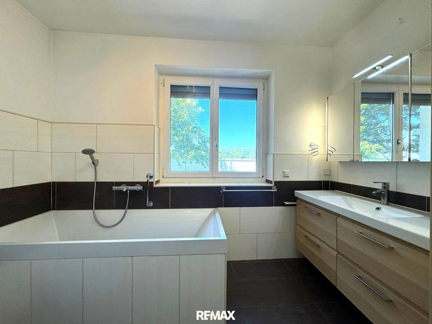 Modernes Badezimmer mit Badewanne, Doppelwaschbecken und Fenster für Tageslicht.