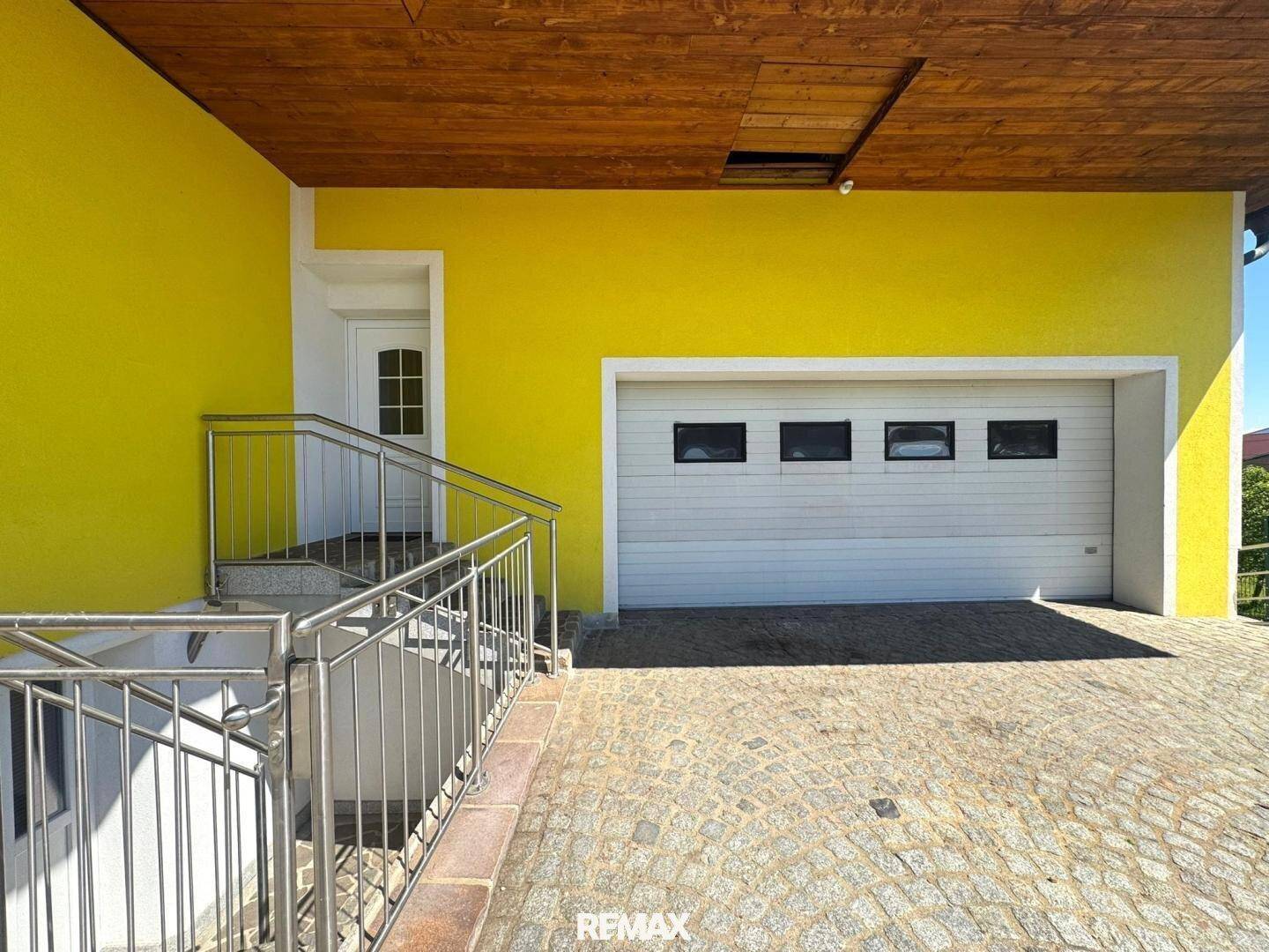 Eingangsbereich mit Treppe und Zugang zur Garage, gepflasterter Vorplatz.