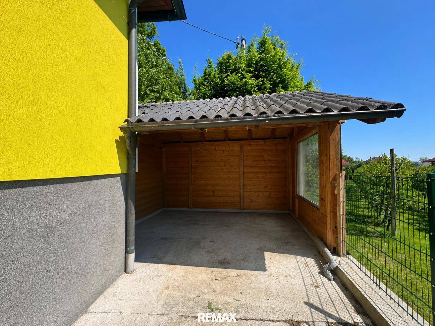 Hölzerner Carport oder Schuppen neben dem gelben Haus, bietet Schutz und Stauraum.