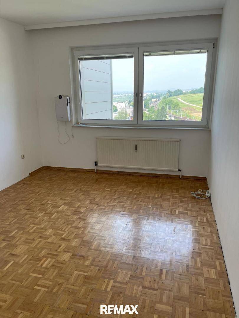 Helles Zimmer mit Parkettboden und großem Fenster, ideal als Schlaf- oder Arbeitszimmer.