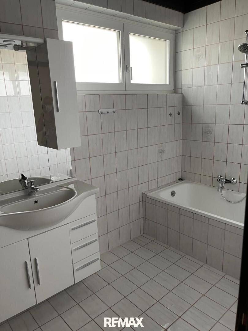 Gefliestes Badezimmer mit Badewanne, Waschbecken und Fenster für natürliche Belüftung.