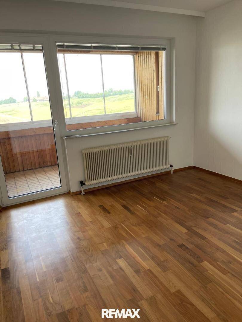 Geräumiges Zimmer mit Parkettboden und Zugang zu einem Balkon, bietet viel Tageslicht.