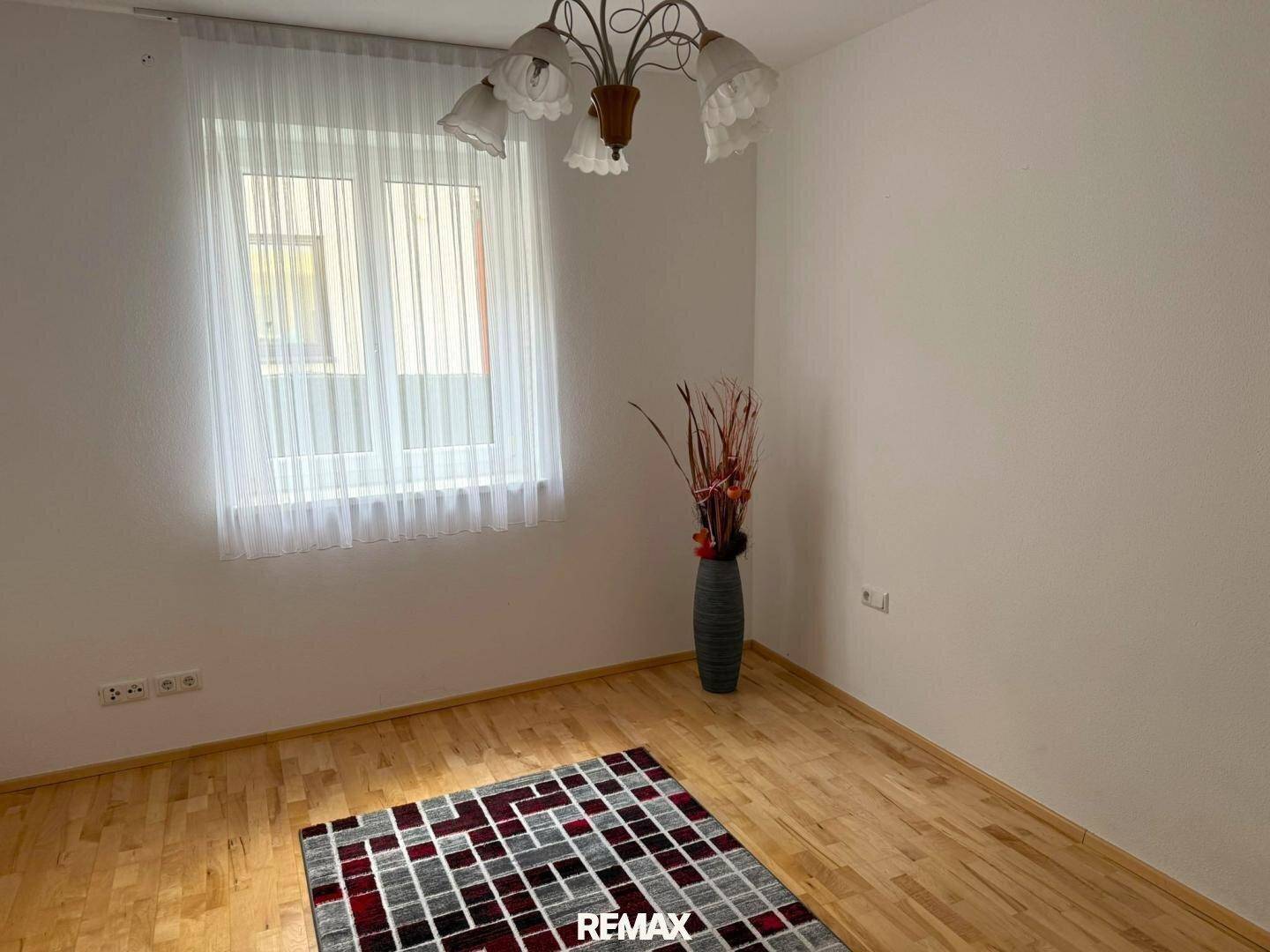 Helles Schlafzimmer mit Holzboden, großem Fenster und dekorativer Vase.