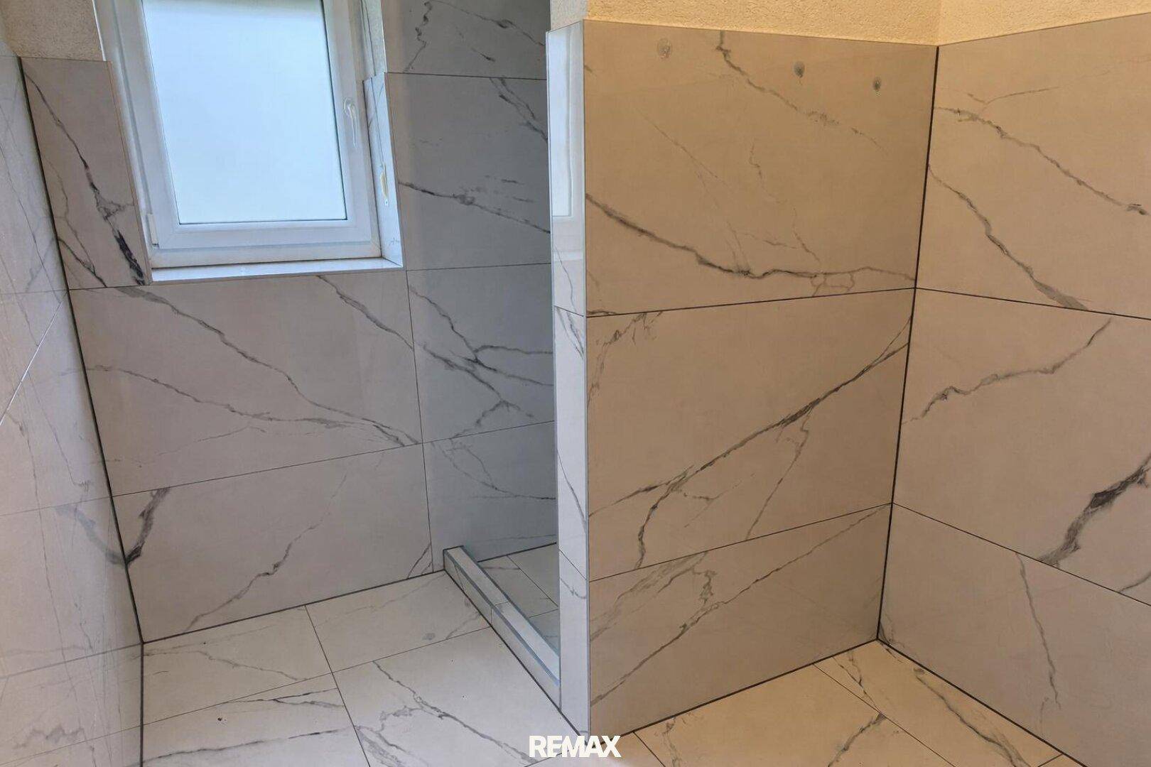 Geräumige begehbare Dusche mit eleganten Marmoroptik-Fliesen und Fenster.