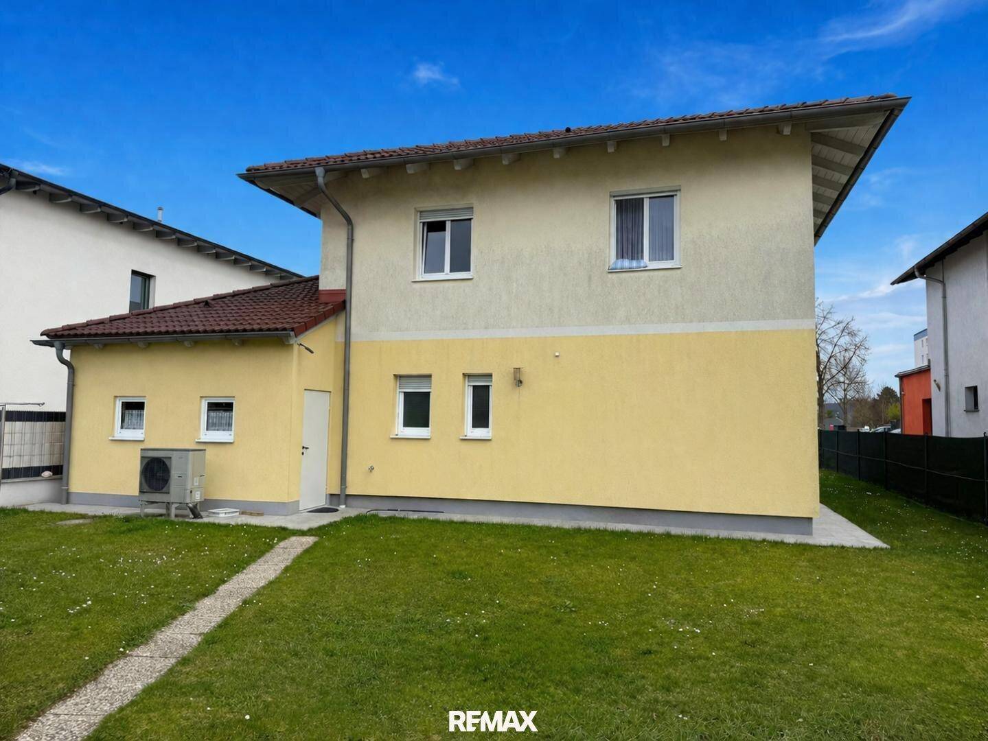 Seitenansicht des Hauses mit Wärmepumpe und gepflegter Rasenfläche.