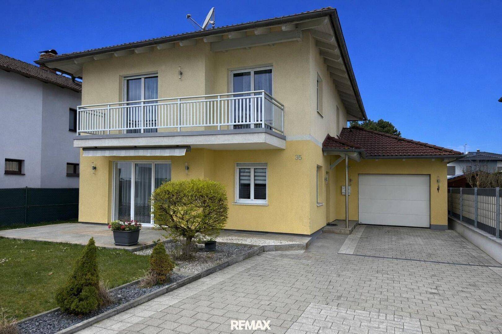 Ansicht des gelben Einfamilienhauses mit Garage, gepflasterter Einfahrt und Balkon.